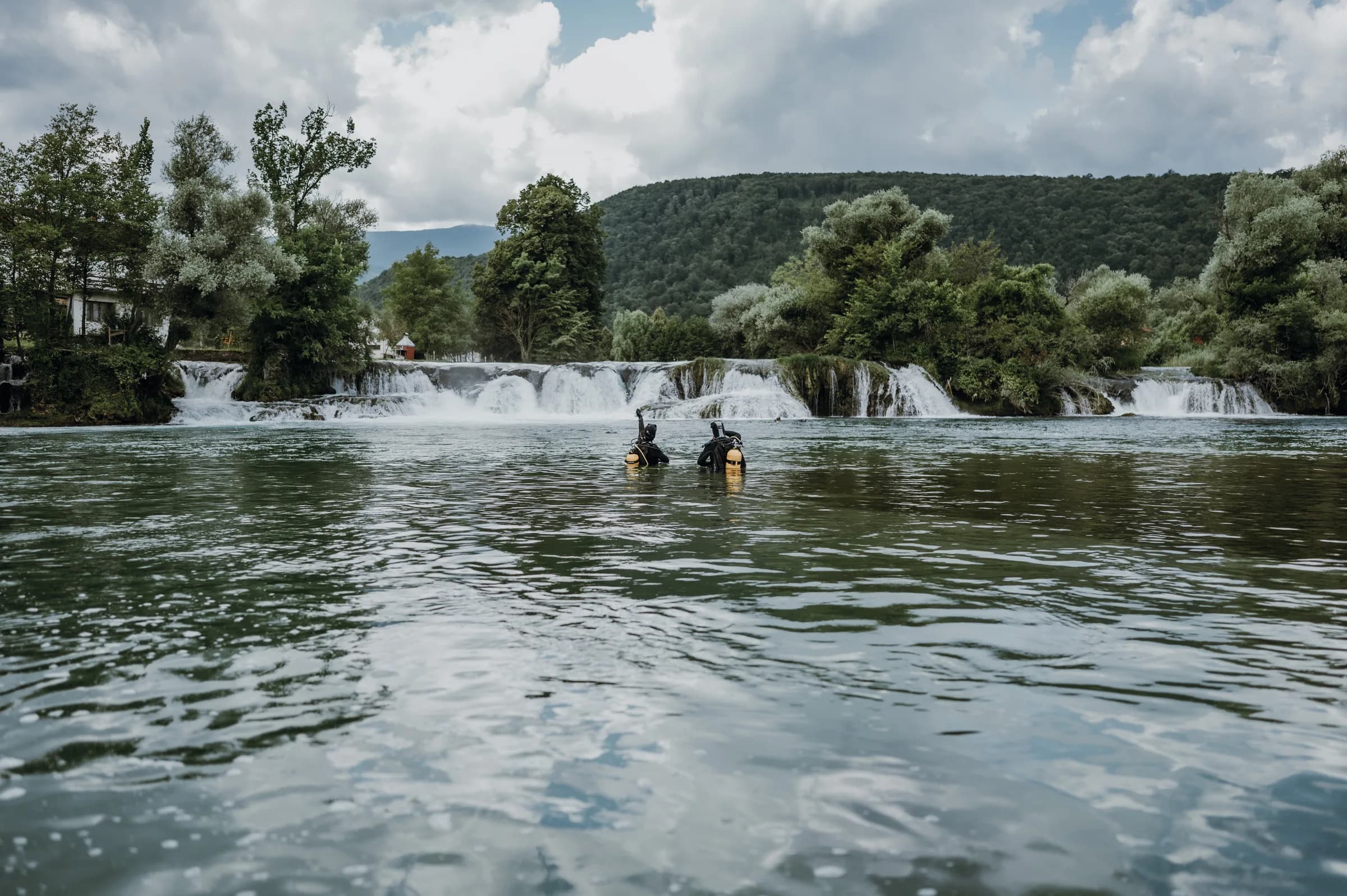 Divers in the Una River near a waterfall during an environmental cleanup action.