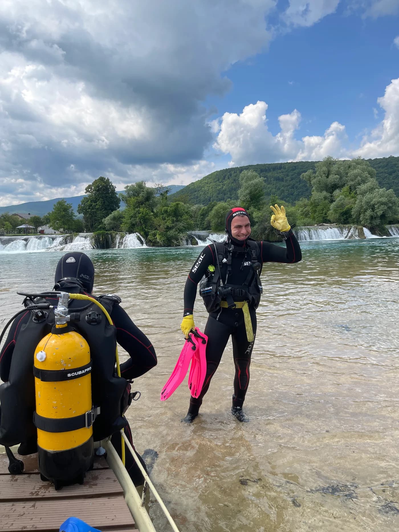 A diver in the Una signalling OK toward the camera, with waterfalls behind.