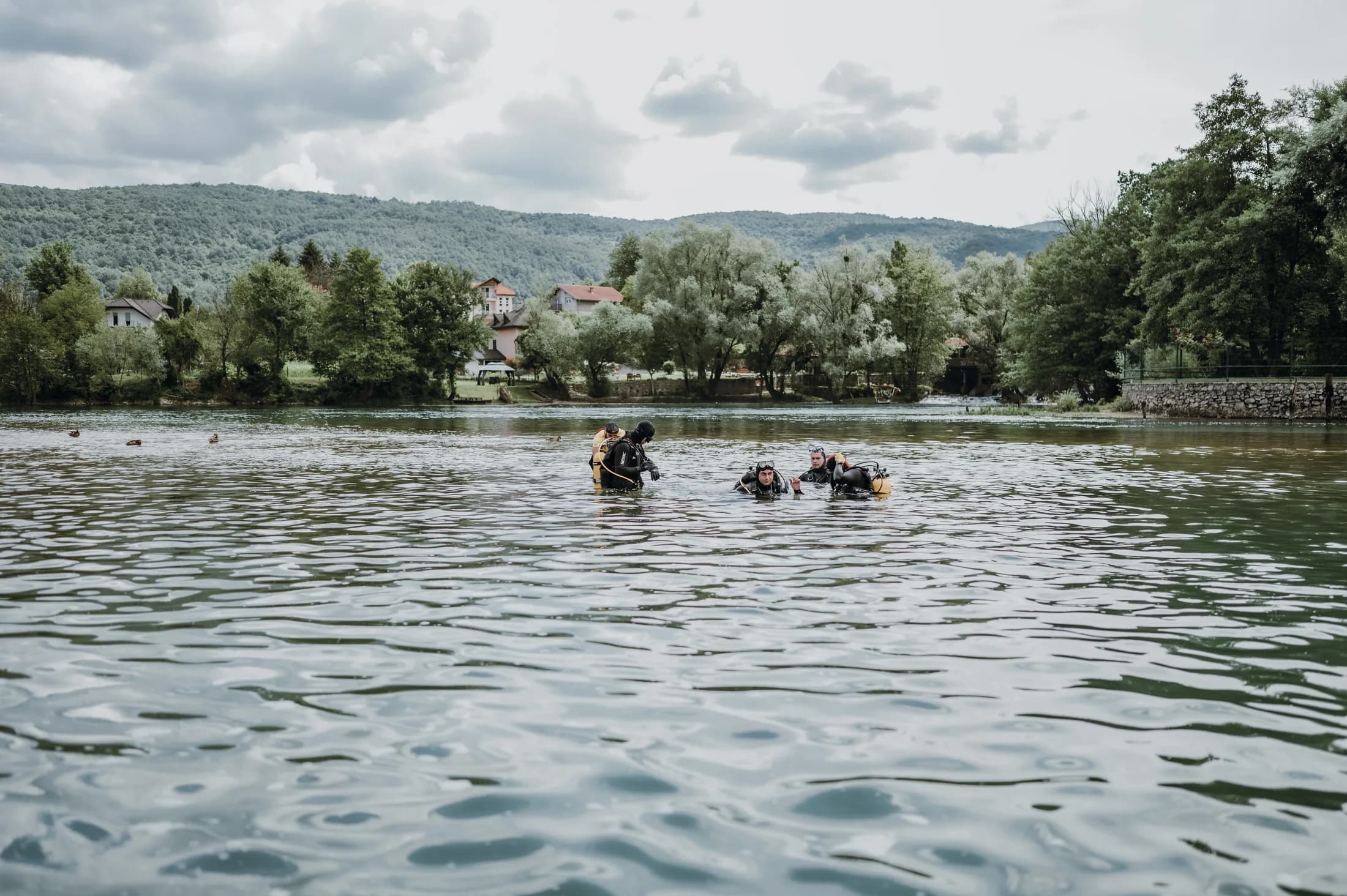 Divers standing in the Una River with forested hills behind them.