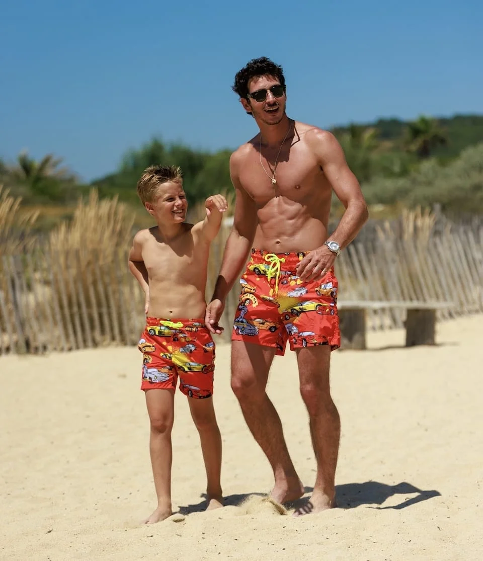 A father and son in matching printed swim shorts on the beach