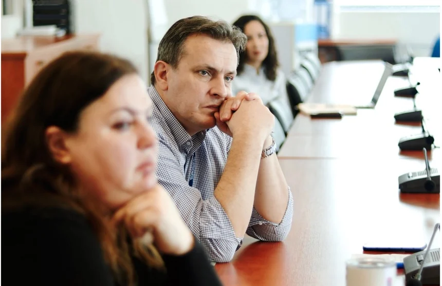Two people listen from along the table, one resting her chin on her hand.