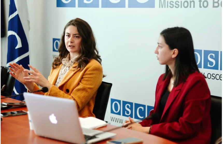 Two women at the head of the table, one speaking with open hands, the other listening.