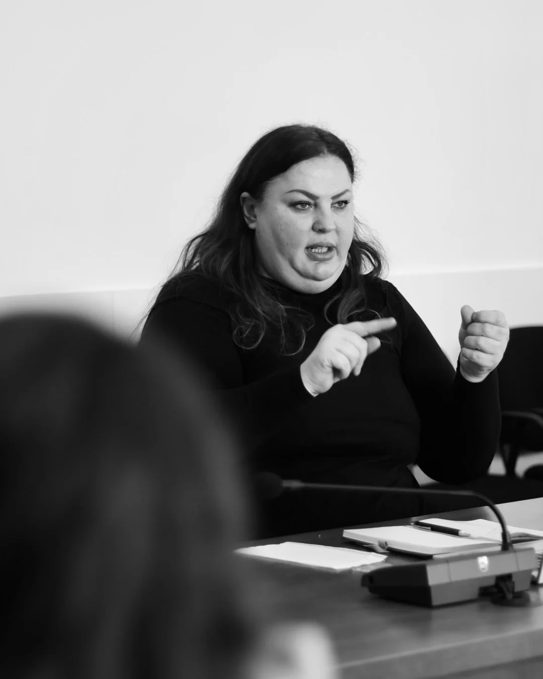 In black and white, a woman makes a point with both hands across the table.