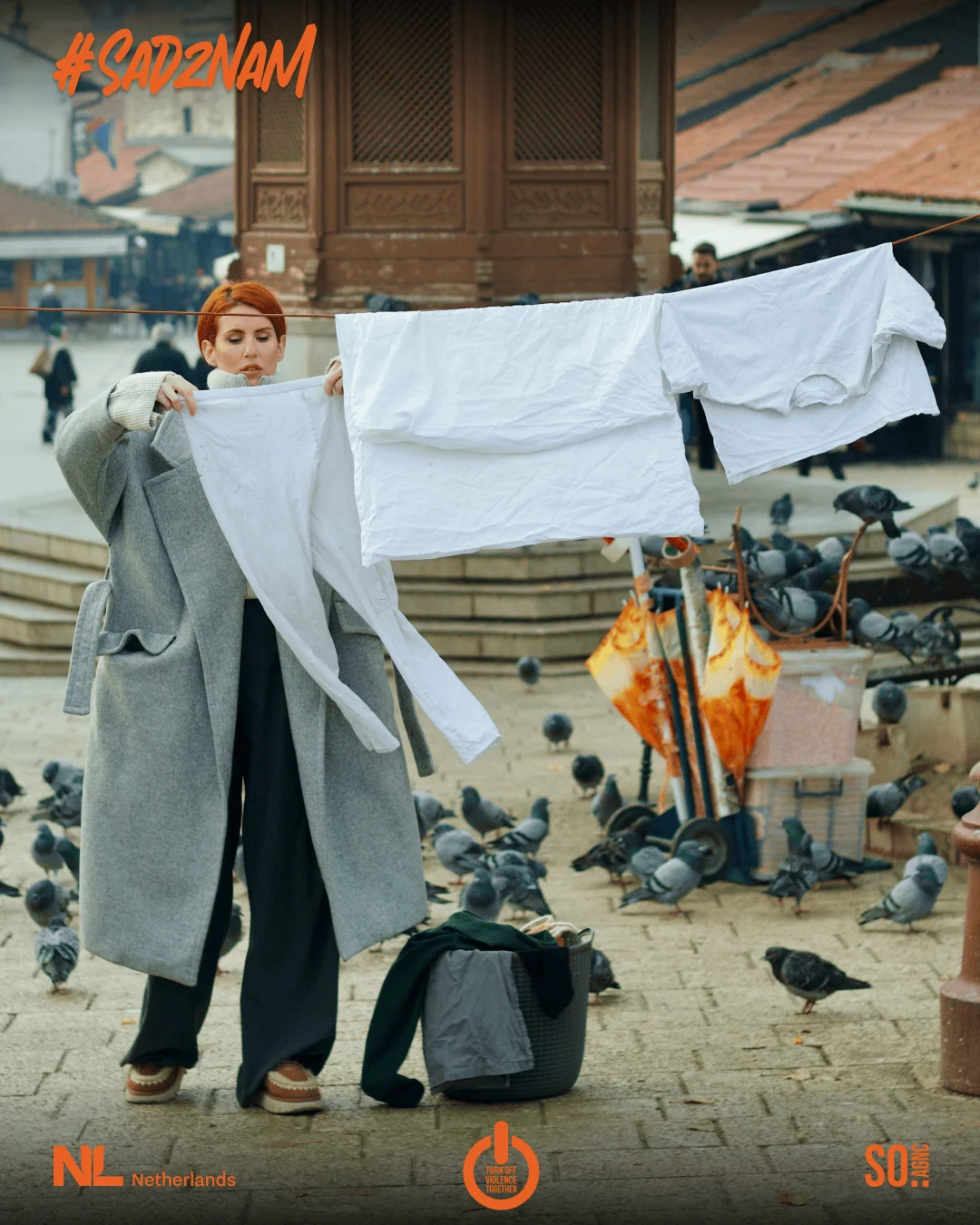 Campaign artwork: a woman in a long grey coat holds out white sheets at the Sebilj, the #SadZnam lettering above her.