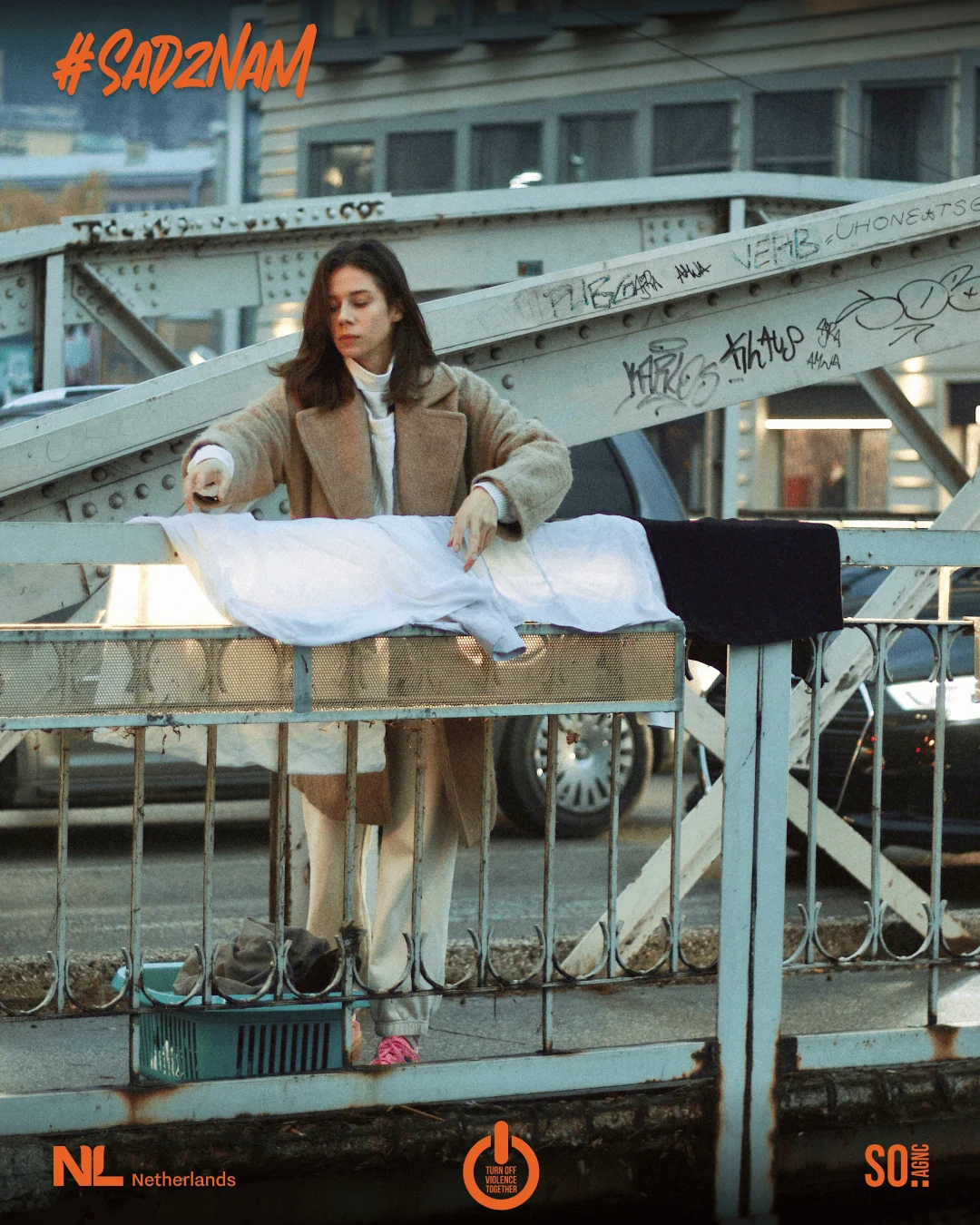 Campaign artwork: a woman behind a bridge railing laying out white linen, the #SadZnam lettering above.