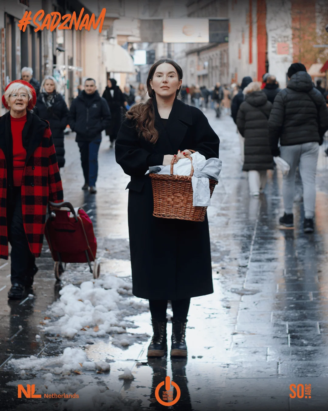 Campaign artwork: a woman in black with a basket on a wet street, passers-by behind her, the #SadZnam lettering above.