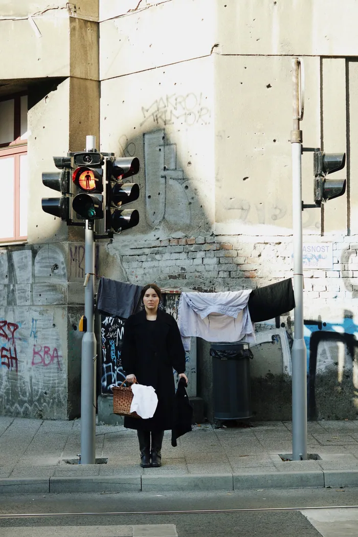 The same street corner, the woman in black holding a basket, the line of washing behind her.