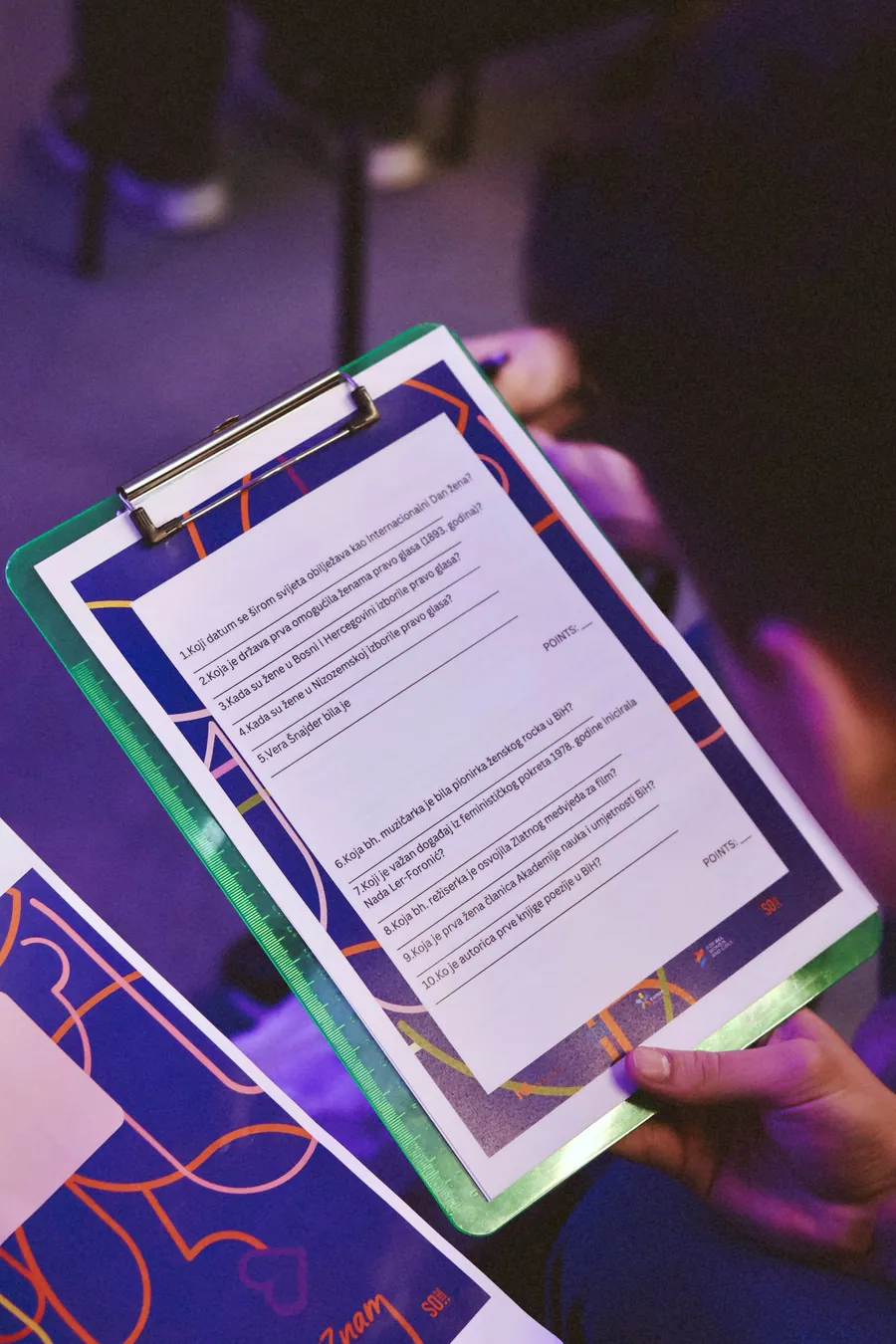 A clipboard held in a hand under coloured light.