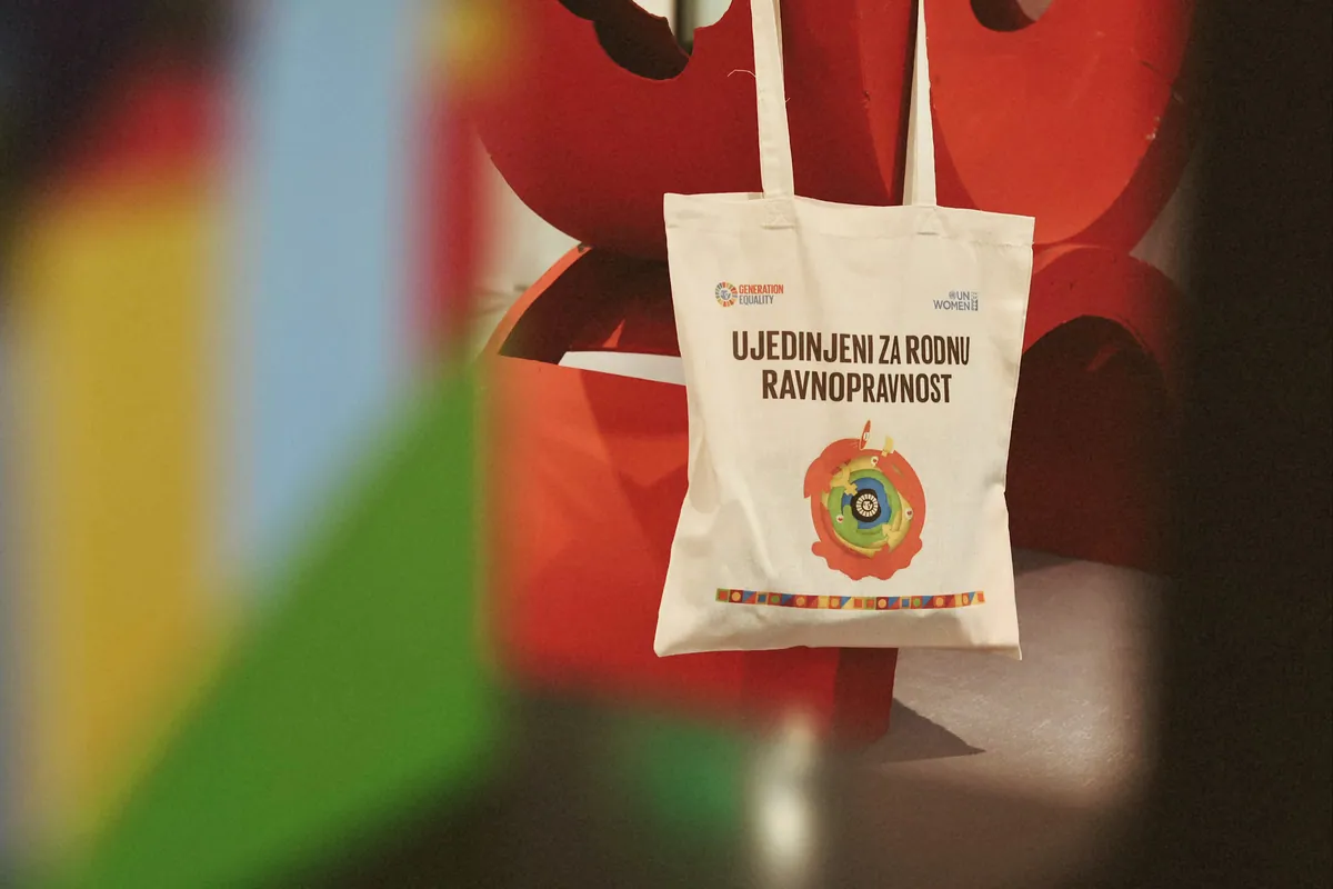 A canvas tote bag with a printed emblem held up against a red cloth.
